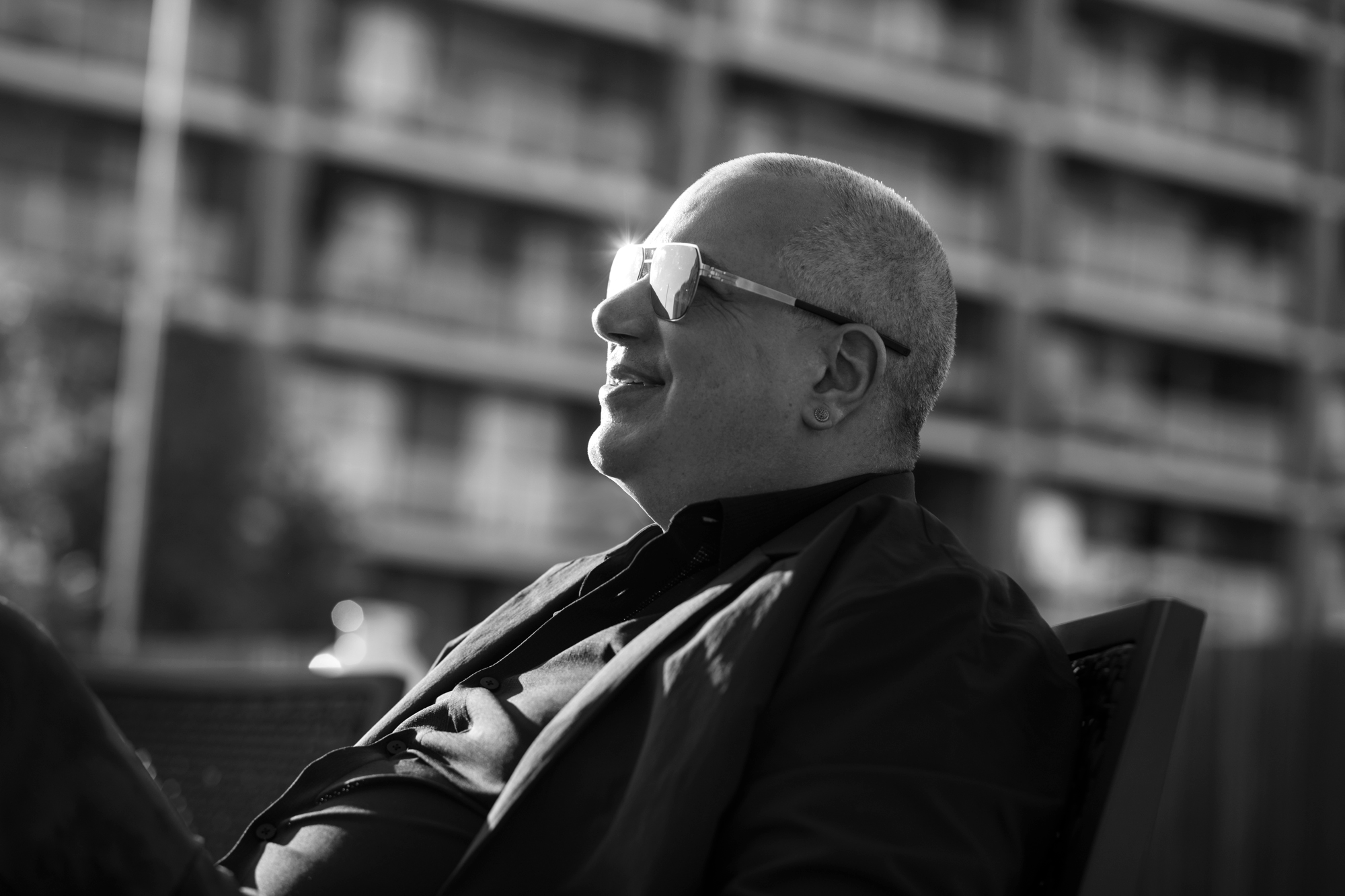 Paul Regan, in profile, black jacket, mirrored sunglasses catching the sun